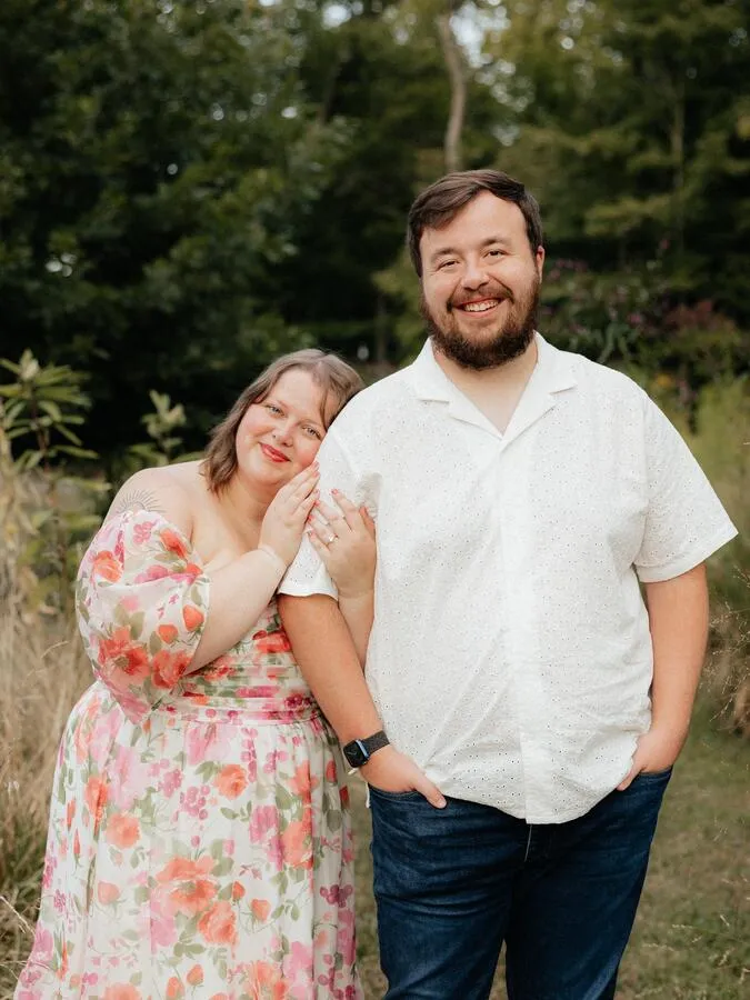 Me with my fiancée Roxanne posing for one of our engagement photos in front of a garden and forest.